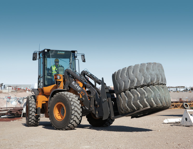 A case loader hauling two large used heavy equipment tires