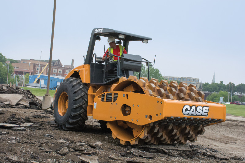 A Case compactor rolling over a dirt mound